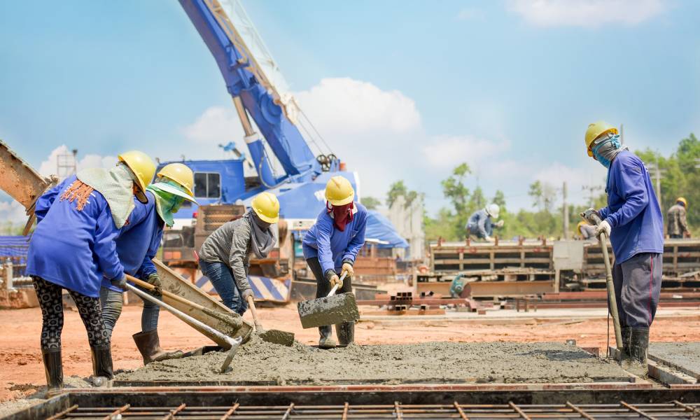 A group of construction workers in protective wear laying down wet concrete on an active construction site.